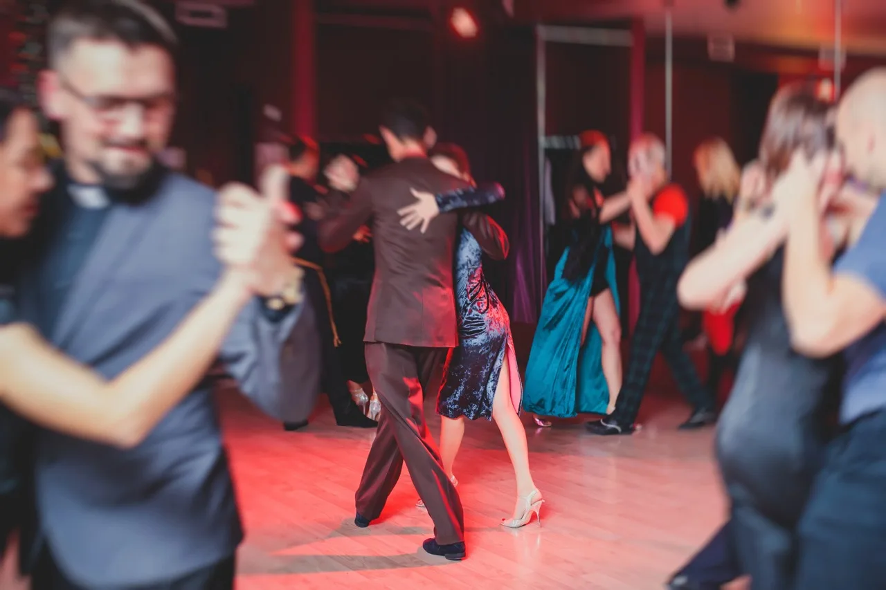 De do’s en don’ts van een milonga: wat je wél en beter niet doet 2 Couples dancing argentinian dance milonga in the ballroom, tango lesson in the red lights, dance festival
